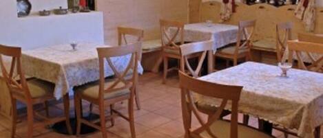 A dining area with multiple tables and chairs, a tiled floor, and hanging pendant lights.