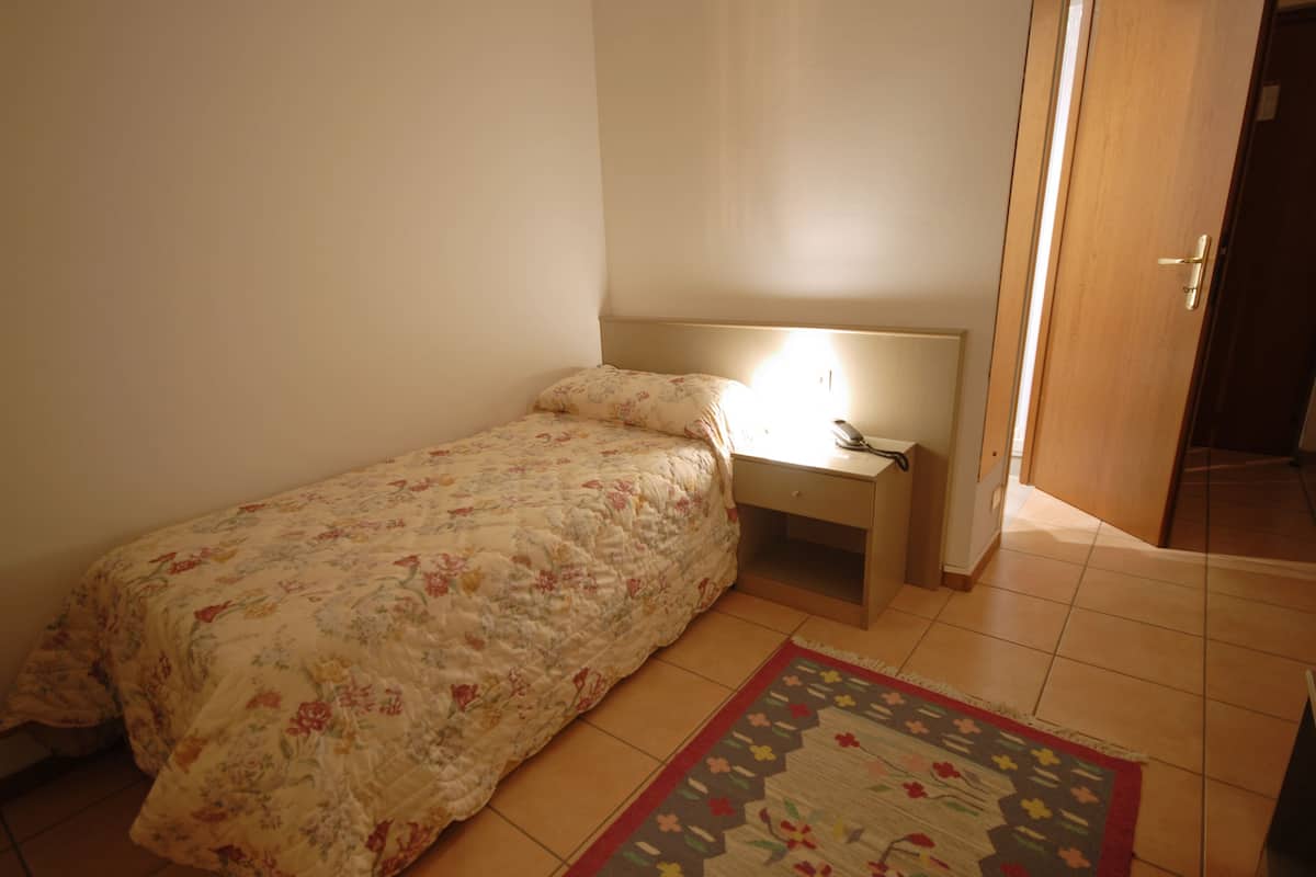 Un dormitorio con una cama individual, una mesita de noche, una lámpara de noche y una alfombra estampada.