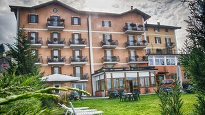 A multi-story hotel with balconies, outdoor seating, and a well-maintained garden. - Stella delle Alpi (Ronzone)