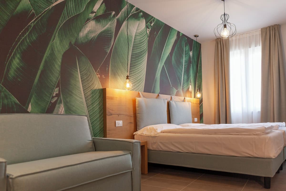Una habitación de hotel con cama, sofá, pared con diseño de hojas y lámpara colgante.
