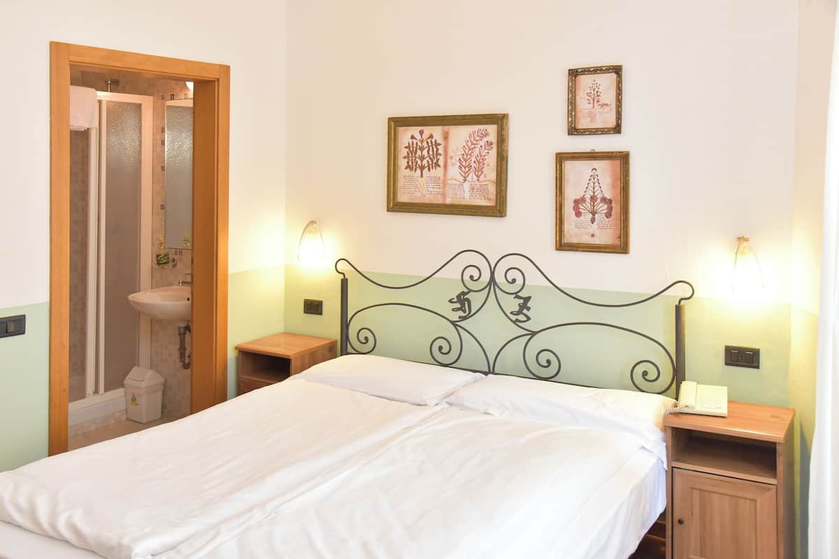 Un dormitorio con cama, mesita de noche, teléfono en la pared e impresiones enmarcadas de motivos botánicos.