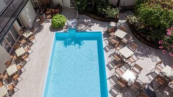 Una piscina en la azotea con un elemento acuático azul, rodeada de mobiliario exterior y plantas en macetas.