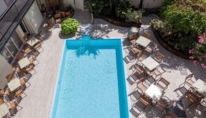 A rooftop pool with a blue water feature, surrounded by outdoor seating and potted plants.