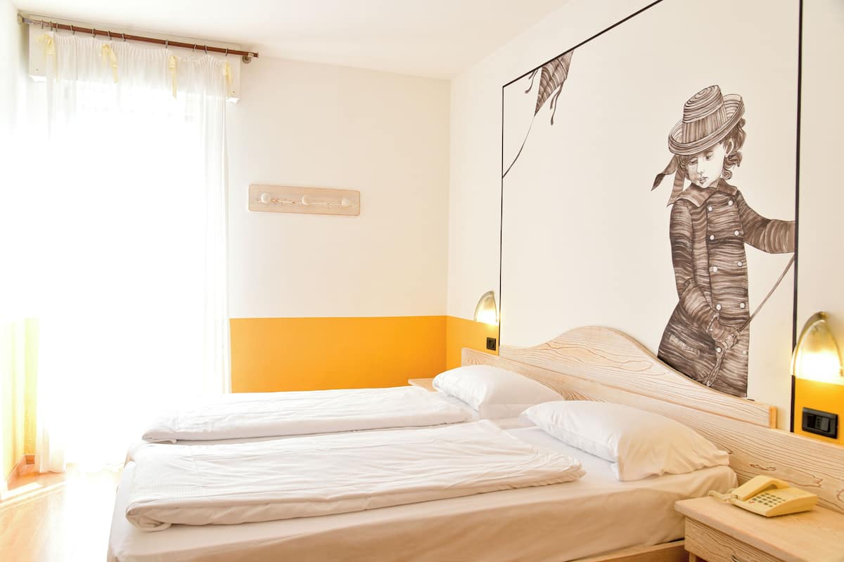 Habitación de hotel con dos camas, un cuadro grande de una persona, cabecero de madera y mesita de noche con un teléfono.