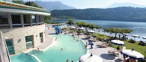 A pool area with a water slide, lounge chairs, umbrellas, and a view of a lake and mountains. - Parc Hotel Du Lac (Levico Terme)