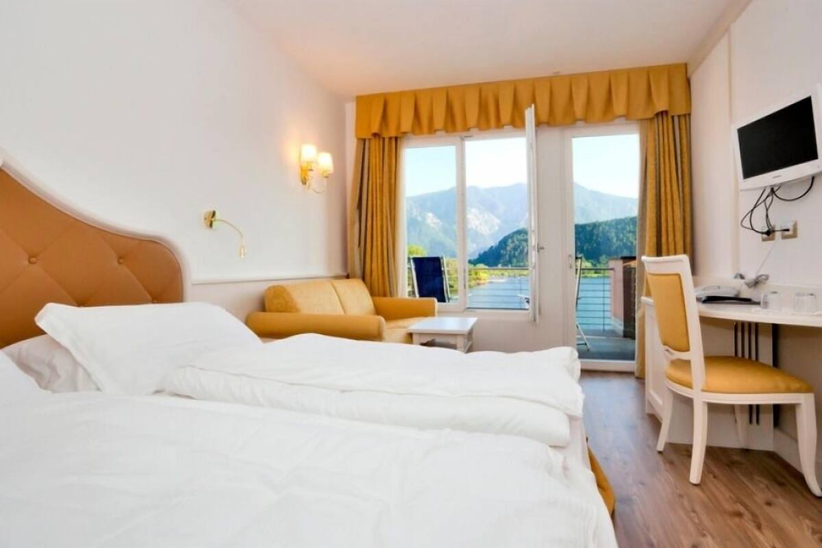 A hotel room with a bed, a desk, a chair, a small table, and a TV.