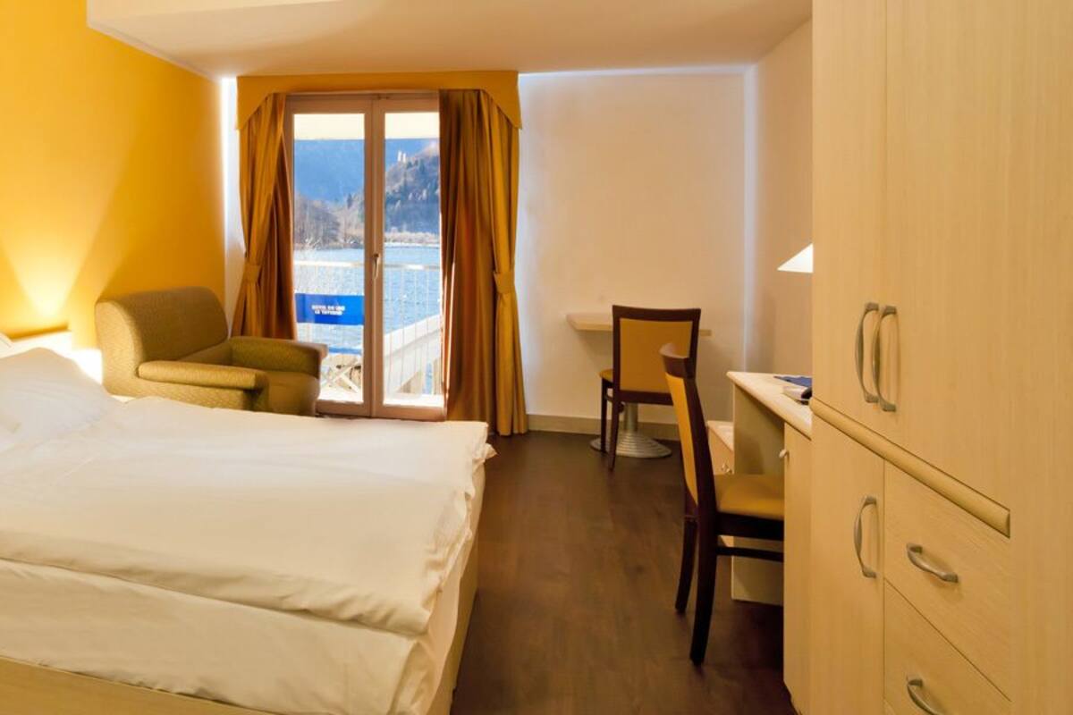 A hotel room with a bed, a desk, a chair, and a view of a body of water through a window.