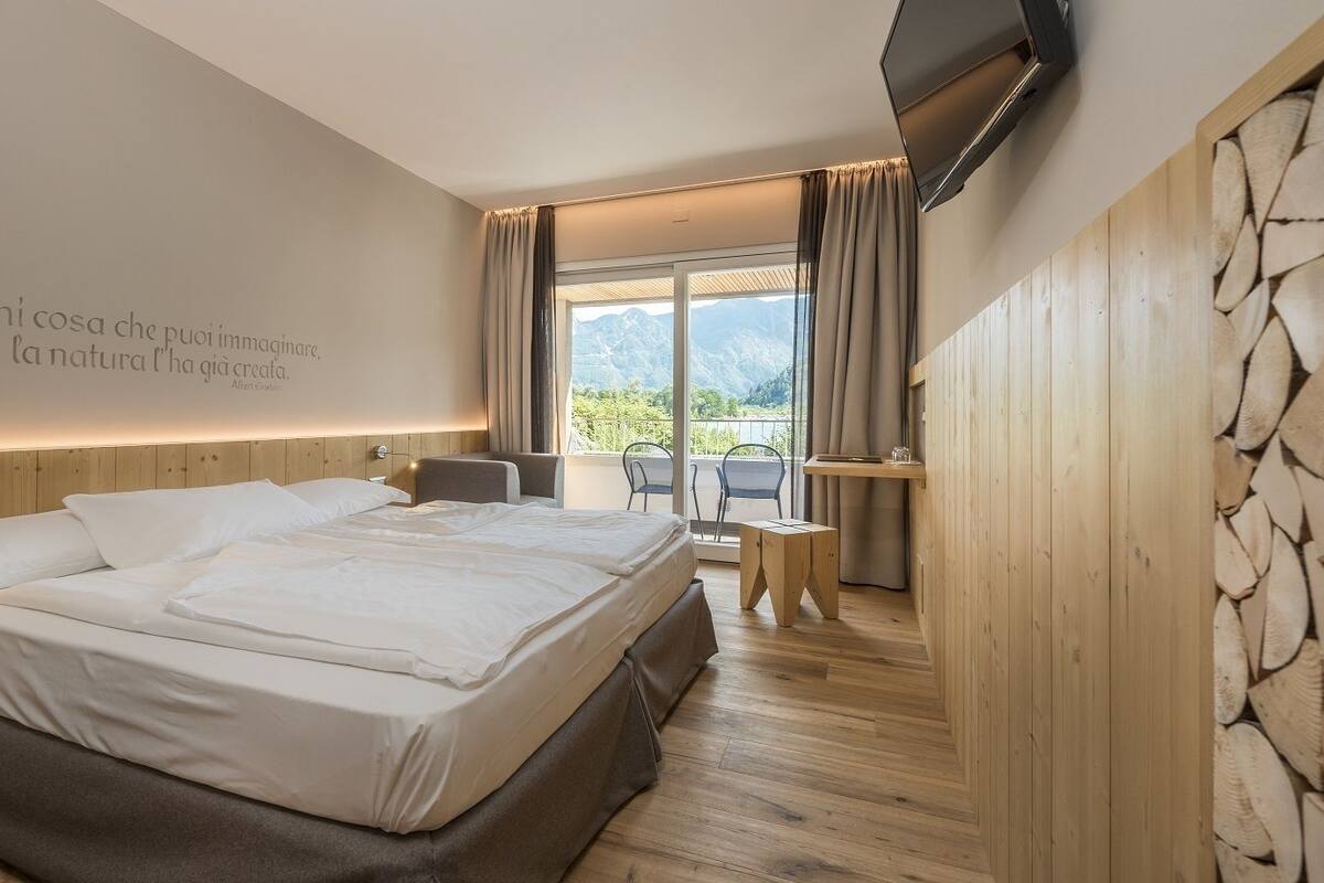 A modern hotel room with a large bed, a desk, and a view of mountains through the window.