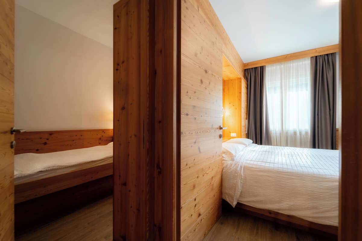 Une chambre de style cabane en bois, avec deux lits simples, une cloison en bois et une grande fenêtre avec des rideaux.
