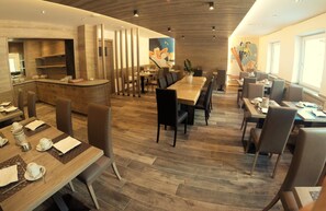 A restaurant with wooden flooring, a central dining table, and a counter with a mural on the wall.