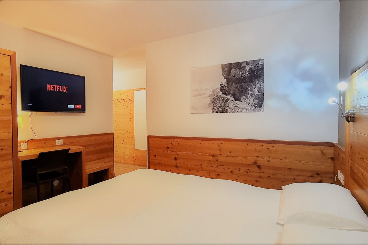 Une chambre à coucher avec un lit, une armoire en bois, un bureau, une chaise, un téléviseur affichant l’interface de « Netflix » et un tableau encadré accroché au mur.