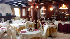 Un comedor de hotel con mesas redondas, manteles blancos y sillas adornadas con cintas blancas y doradas.
