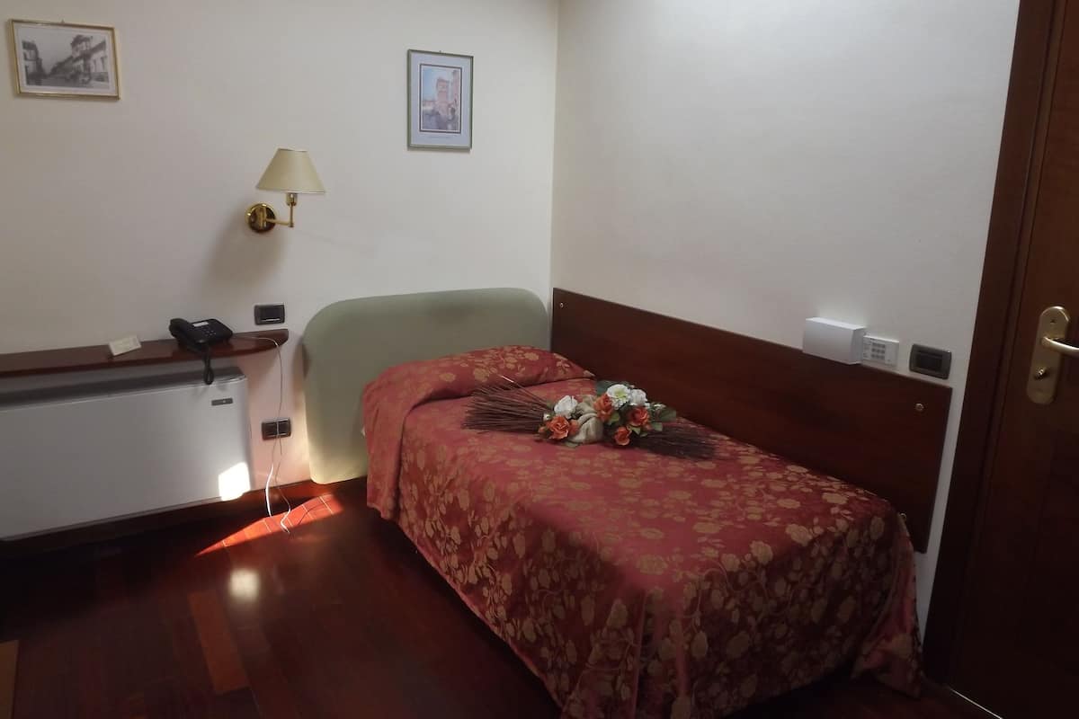 A hotel room with a bed, a desk with a telephone, a lamp, and a wall-mounted thermostat.