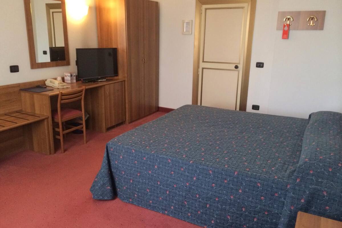 A hotel room with a bed, a desk with a chair, a television, and a wardrobe.