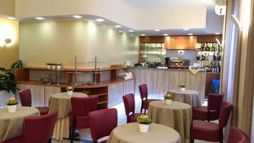 Ein Restaurant mit runden Tischen, roten Stühlen, einer Bar und einer Küche im Hintergrund.