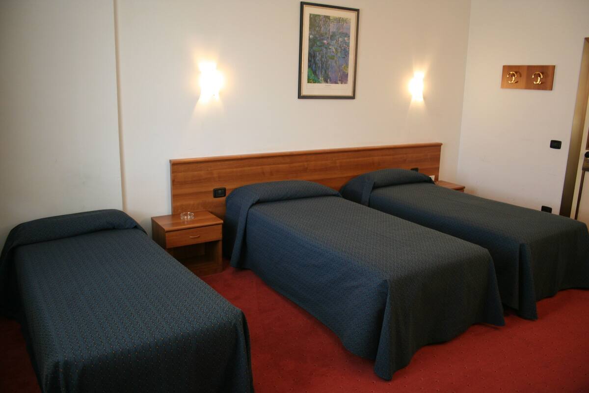 A hotel room with two single beds, a wooden headboard, a small bedside table, and a framed picture on the wall.