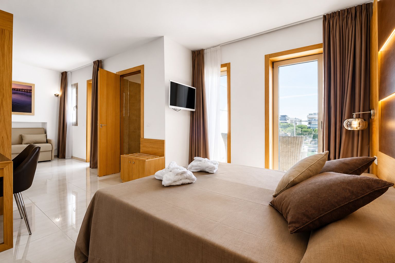A hotel room with a bed, a TV, a desk, and a view of the city.