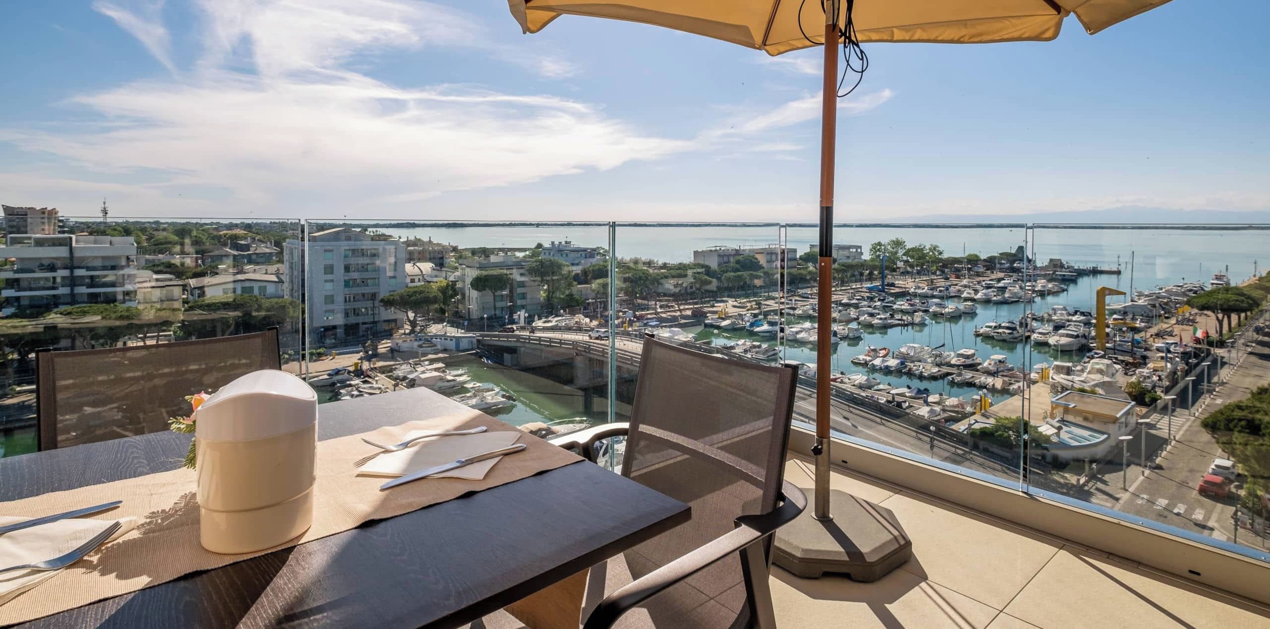 A balcony with a table set for dining, overlooking a marina with boats and buildings.