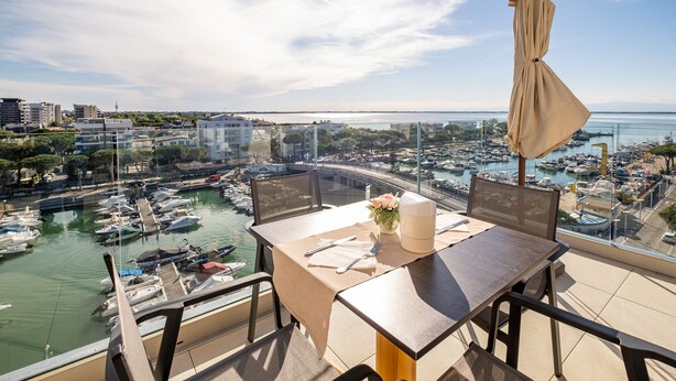 Un balcón con mesa lista para comer, con vista a una marina con barcos y un puente.