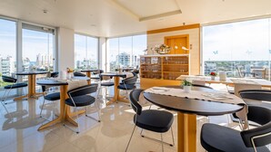 Un comedor moderno con mesas, sillas, ventanas amplias y vistas a la ciudad.