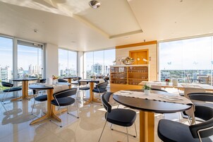 Un'area pranzo moderna con tavoli e sedie, ampie finestre e vista sulla città.
