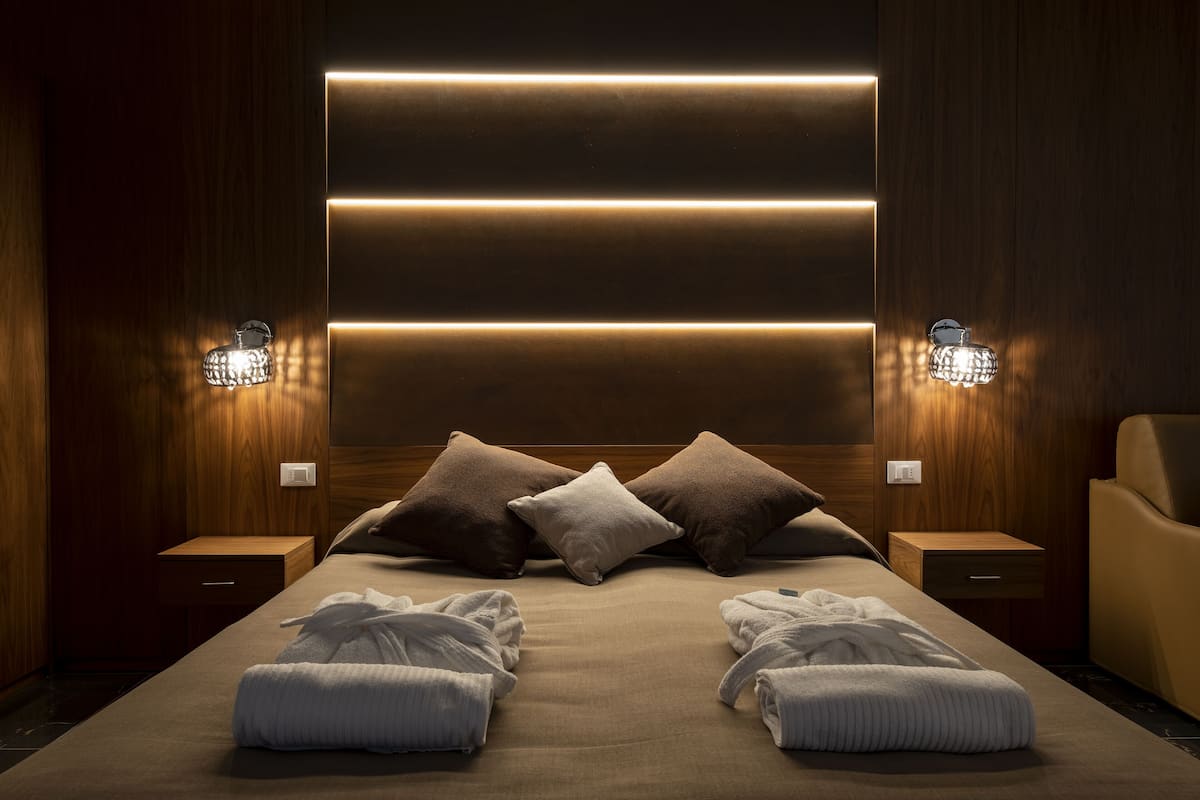 A modern hotel room with a large bed, wooden headboard, and bedside tables.