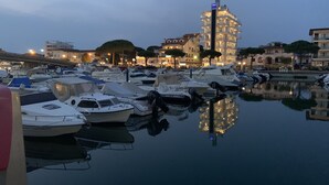 Un puerto deportivo con varias embarcaciones amarradas, un edificio amplio con múltiples balcones y una superficie acuática tranquila que refleja el entorno.