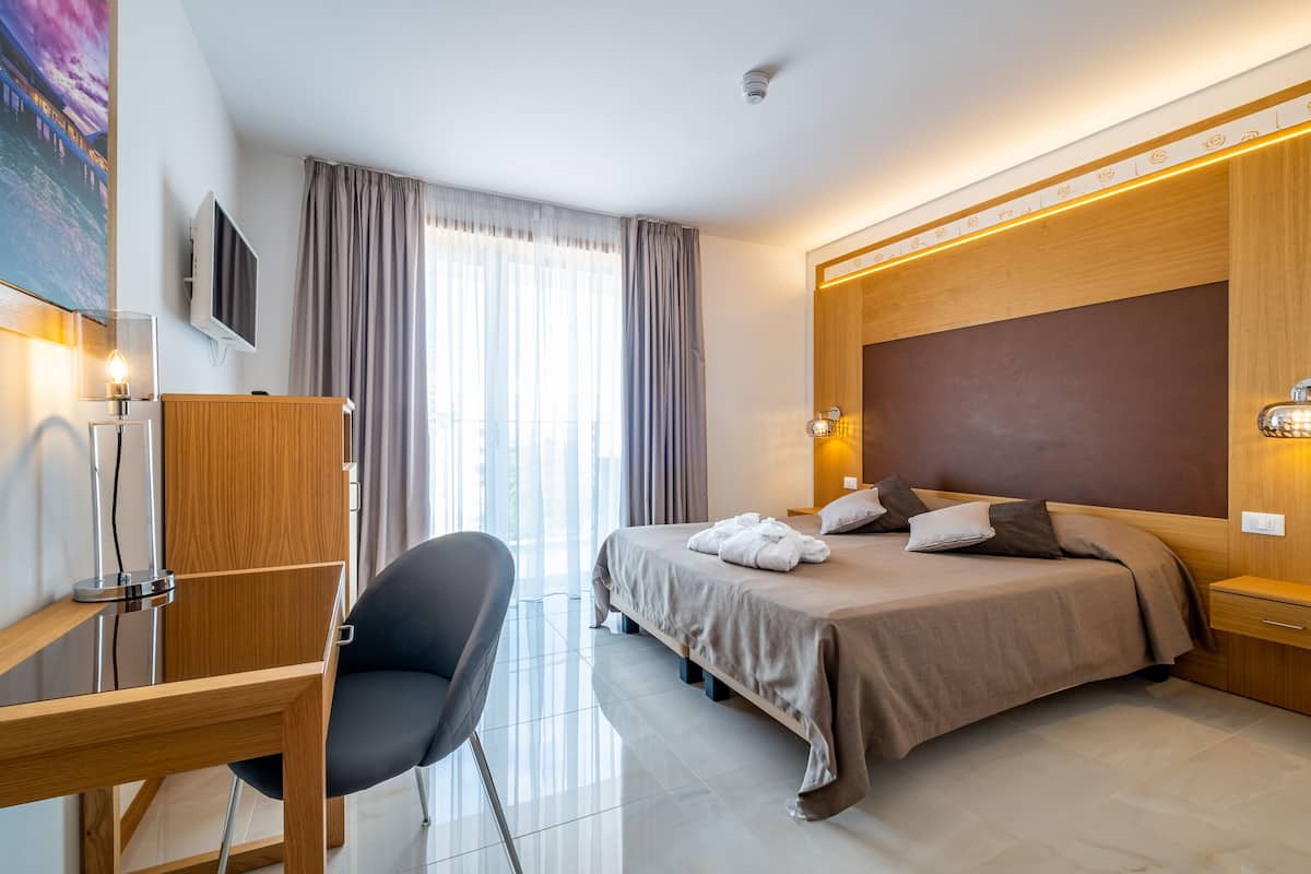 A modern hotel room with a bed, bedside table, chair, and a TV mounted on the wall.