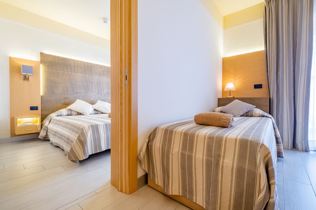 A hotel room with two beds, a wooden headboard, a nightstand with a lamp, and a view of the outdoors.
