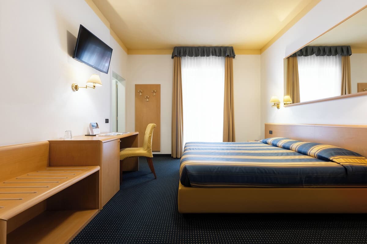 Hotellihuone, jossa on sänky, työpöytä, tuoli, televisio ja peili.