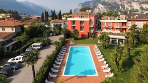 A resort with a swimming pool surrounded by lounge chairs, a parking area, and buildings with balconies. - Hotel Brione Green Resort (Riva del Garda)