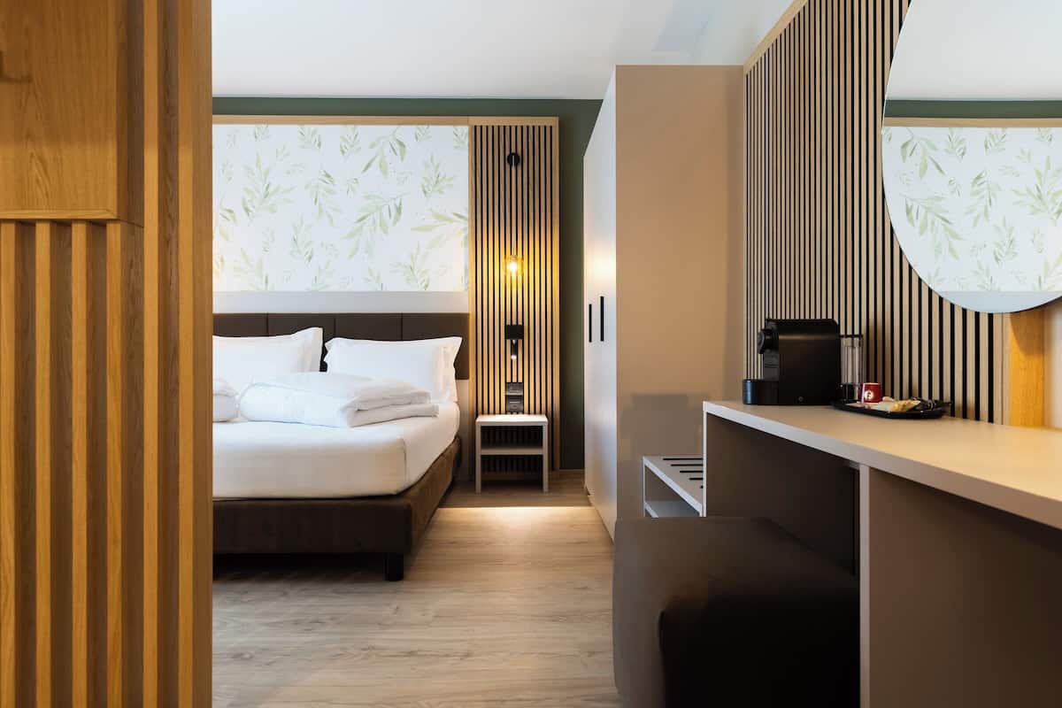 Moderni hotellihuone, jossa on sänky, yöpöytä ja pieni oleskelualue.