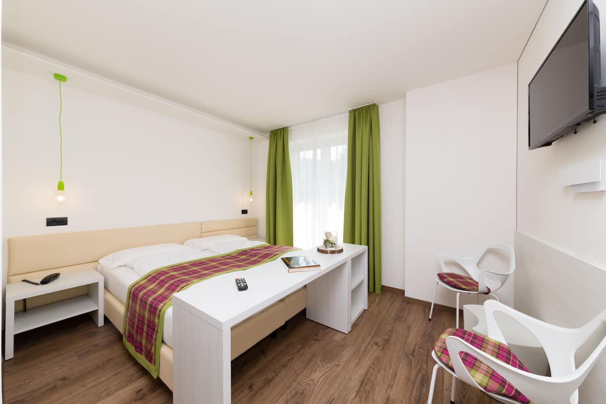 Moderni hotellihuone, jossa on sänky, yöpöytä, tuoli, työpöytä ja televisio.