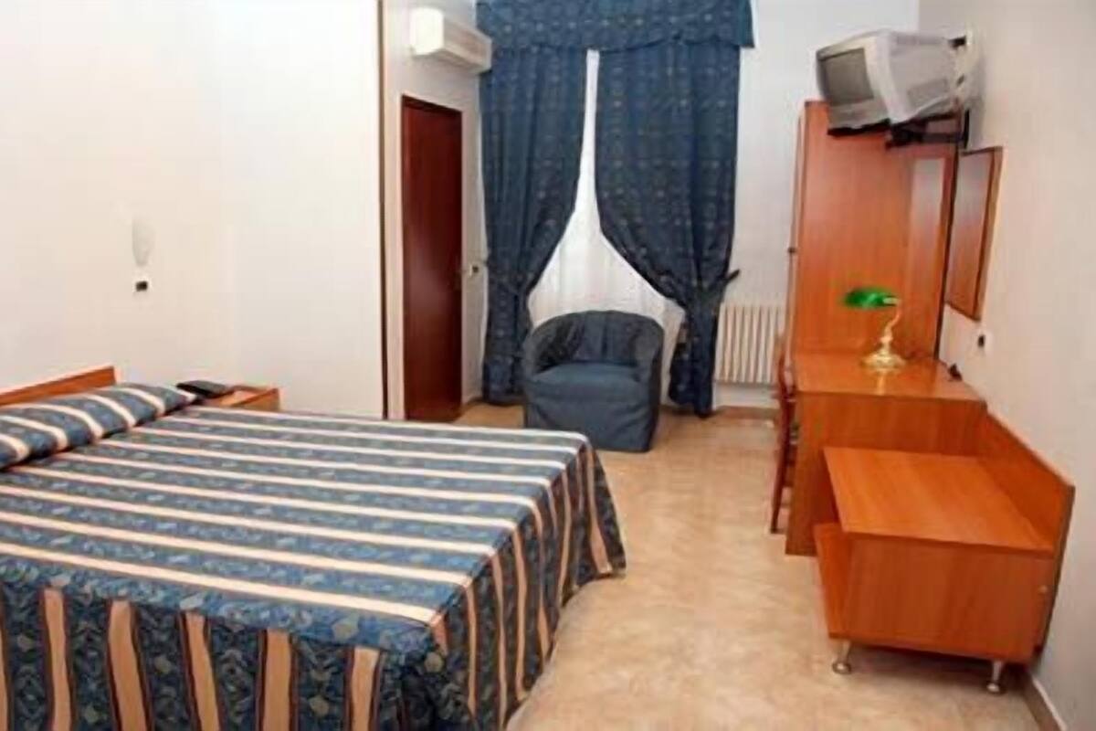 Un dormitorio con una cama doble, un aparador de madera, una silla y un radiador.