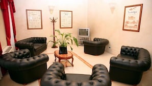 Un salon avec quatre canapés en cuir noir disposés en demi-cercle, une table basse en bois, une plante en pot, un téléviseur et des certificats encadrés accrochés au mur.