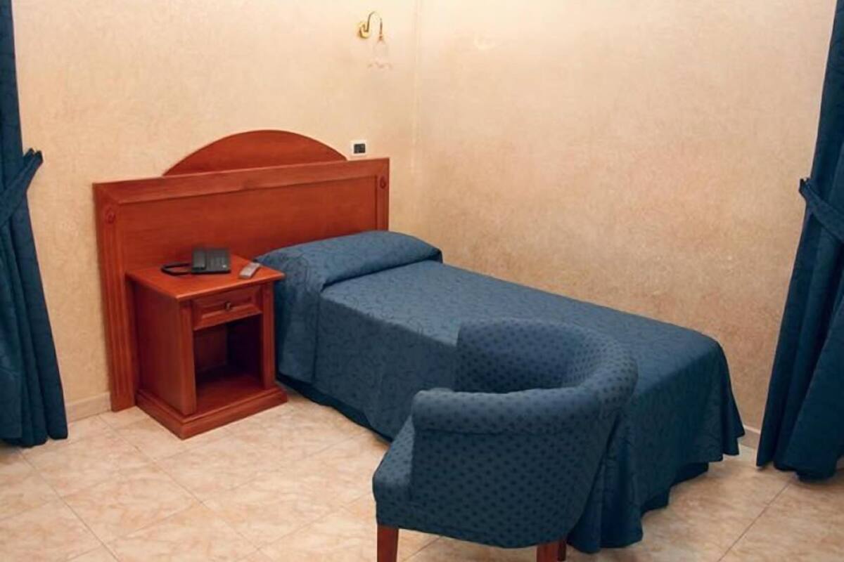 Una habitación pequeña con una cama individual, cabecera de madera, mesita de noche y una silla.