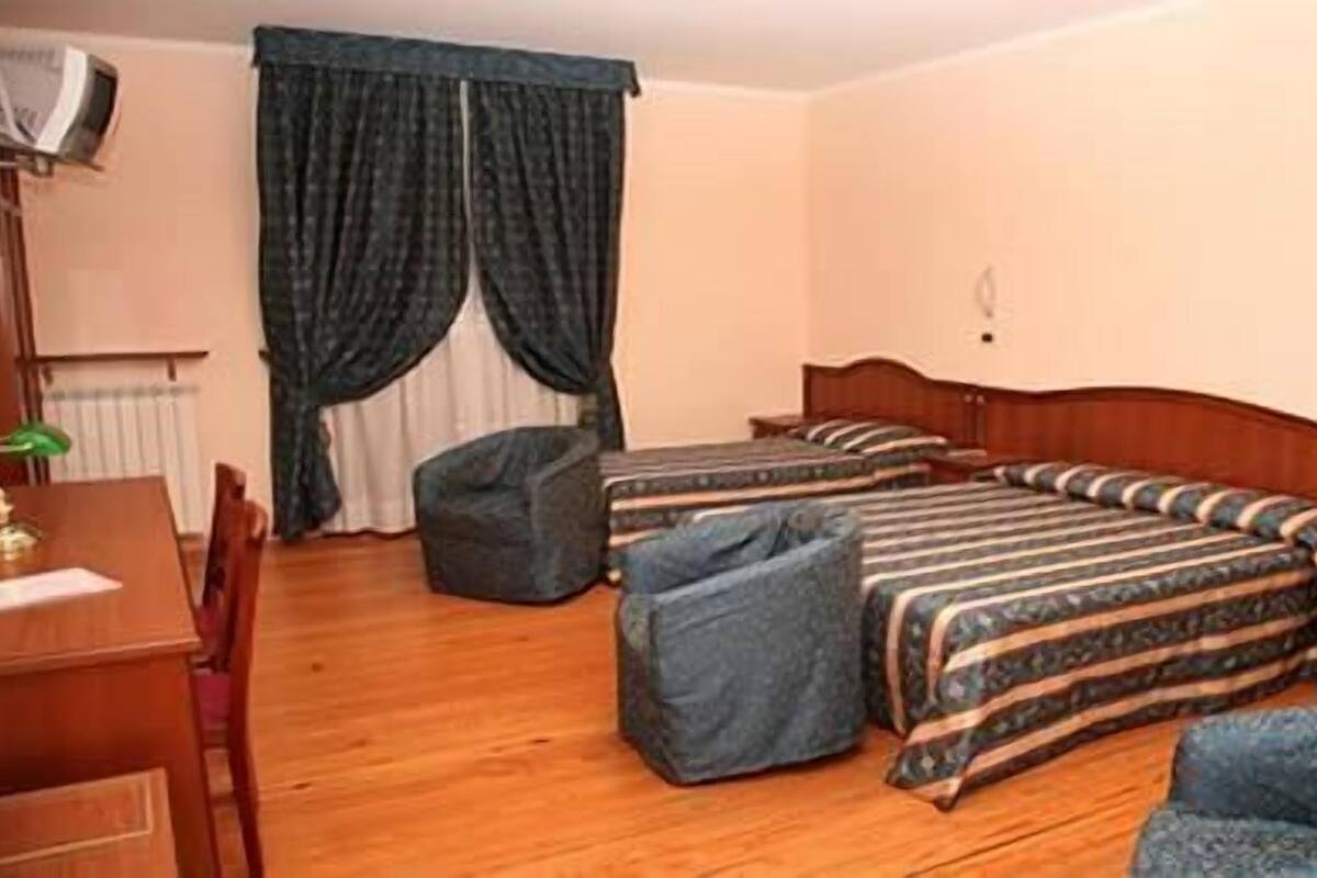 Una habitación de hotel con dos camas individuales, un cabecero de madera, un escritorio con una silla, una mesita y una silla.