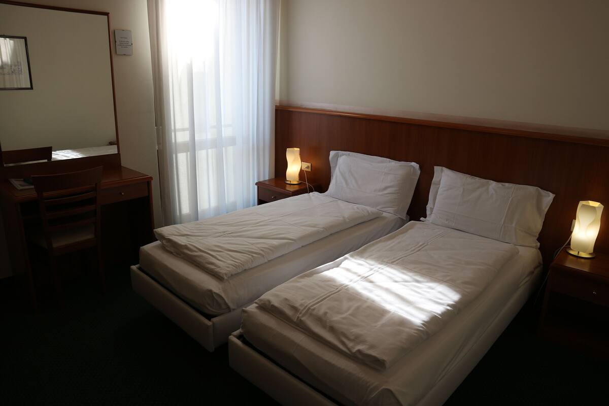A hotel room with two single beds, a desk, and a chair.