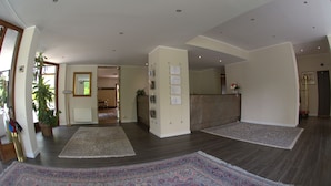 A spacious living area with dark wooden flooring, large rugs, and a reception desk.