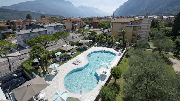 A swimming pool with lounge chairs and umbrellas, surrounded by buildings and mountains.
