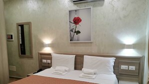 A hotel room with a bed, two bedside tables, a nightstand, a mirror, and a framed picture of a rose on the wall. - Hotel Orchidea (Turin)