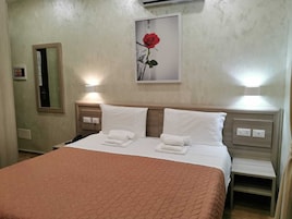 A hotel room with a bed, two bedside tables, a nightstand, a mirror, and a framed picture of a rose on the wall.
