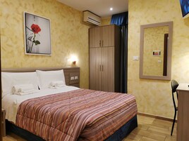 Una camera d'albergo con un letto, un armadio, una scrivania e uno specchio.