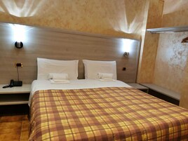 Habitación de hotel con una cama grande, dos mesitas de noche, un teléfono y una lámpara fijada a la pared.