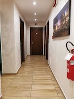 A hallway with wooden flooring, a fire extinguisher mounted on the wall, and a door at the end.