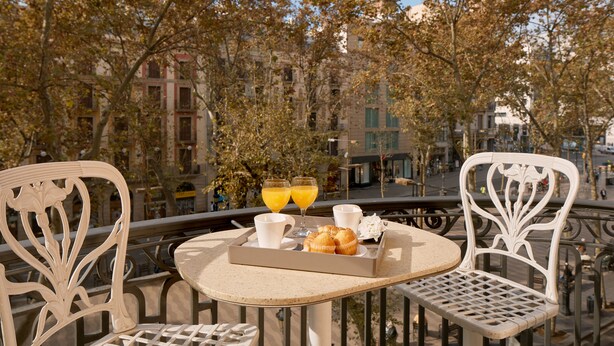 Un balcón con una mesa dispuesta para el desayuno, incluyendo cruasanes, jugo y café.