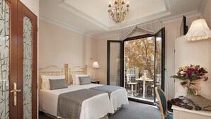 Habitación de hotel con cama, escritorio, silla, candelabro y vista al exterior.
