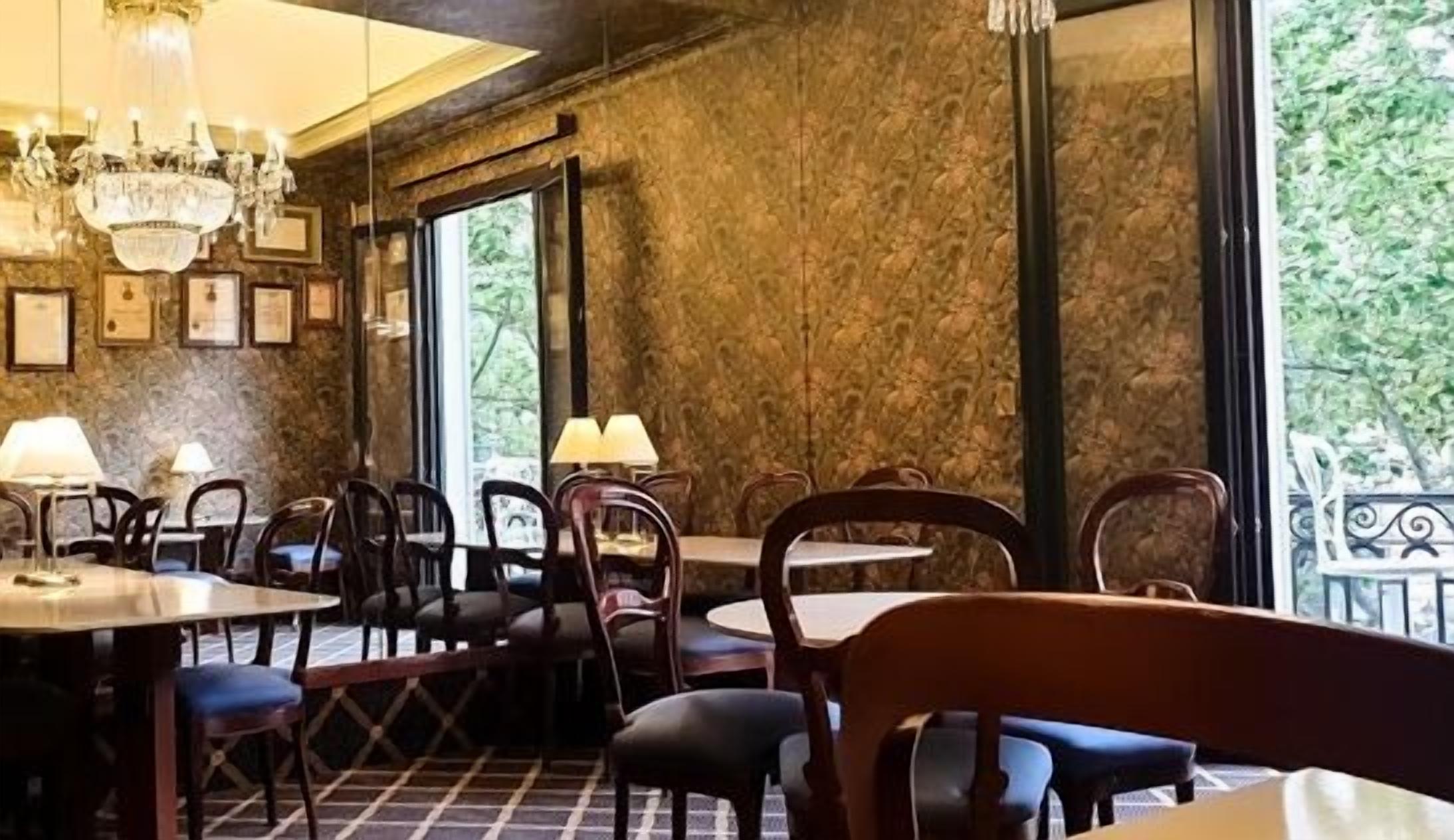 A restaurant with wooden tables and chairs, chandeliers, and a stone wall.