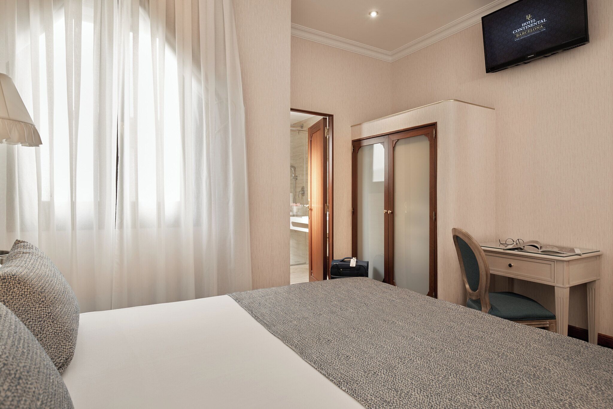 A hotel room with a bed, a desk, a chair, a television, and a wardrobe.