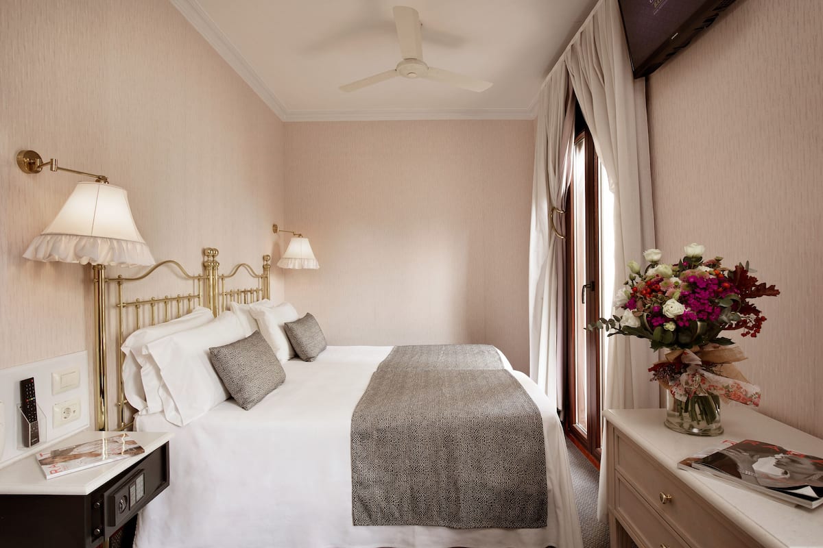 A hotel room with a bed, bedside lamps, a nightstand, a dresser, a vase with flowers, and a ceiling fan.